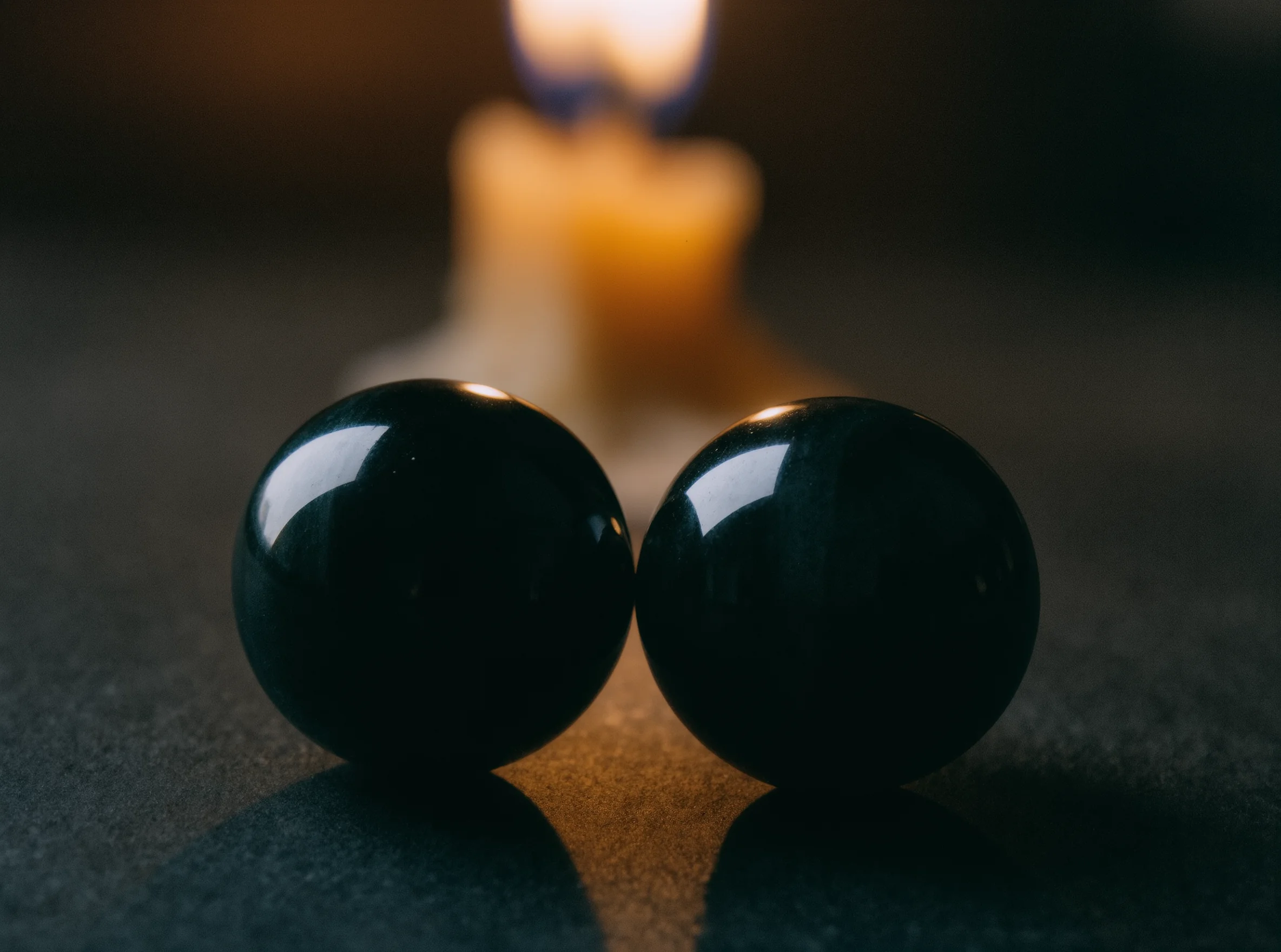 The Prism of Grace: How Light Inhabits the Stone 2 Sacred Light by Yuano: Two obsidian spheres reflecting candlelight in a dramatic chiaroscuro setting
