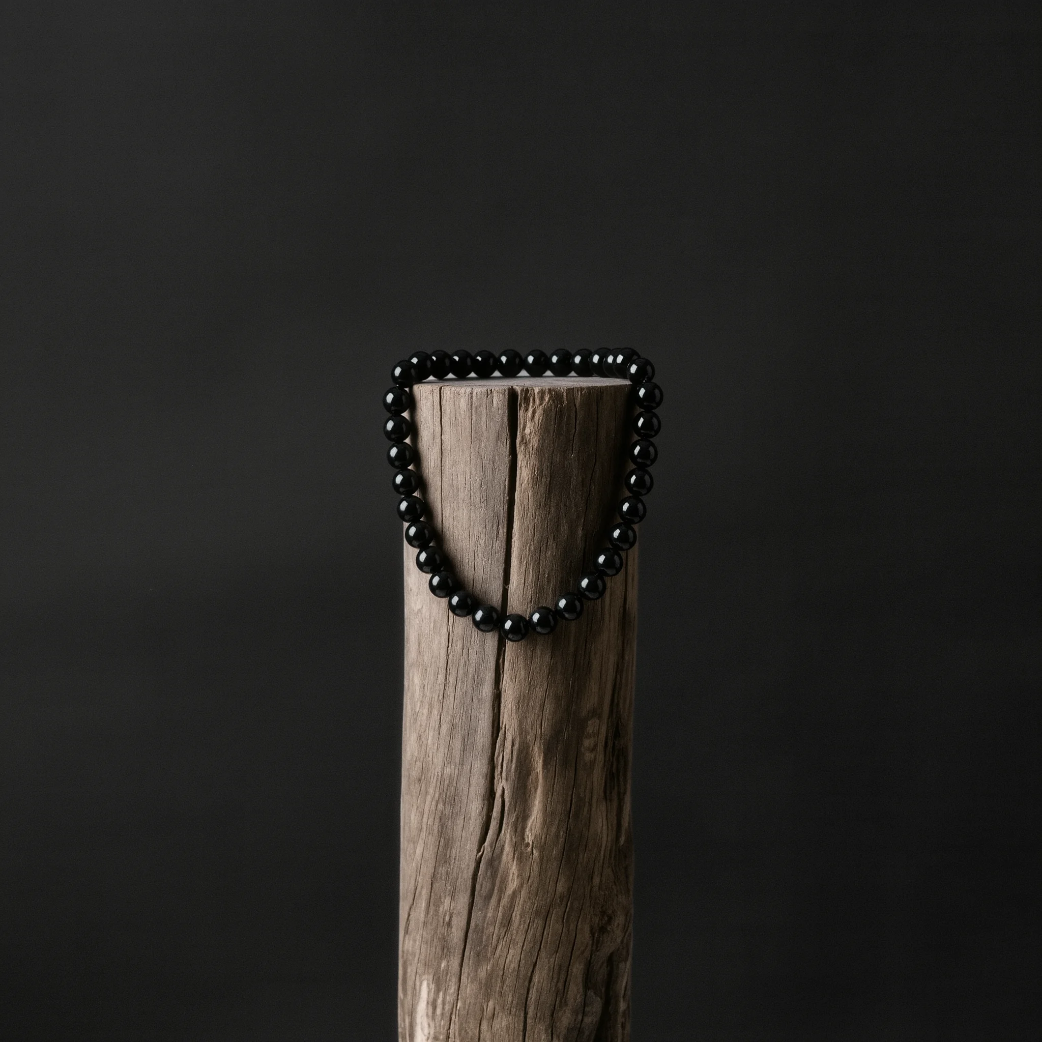 The Work of Mercy 1 Sovereign Stillness Jewelry Values: An obsidian relic anchored on a wooden pillar, symbolizing creation care.